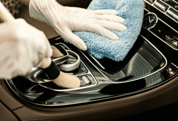 White-gloved hands cleaning a premium car interior centre console with a microfibre cloth