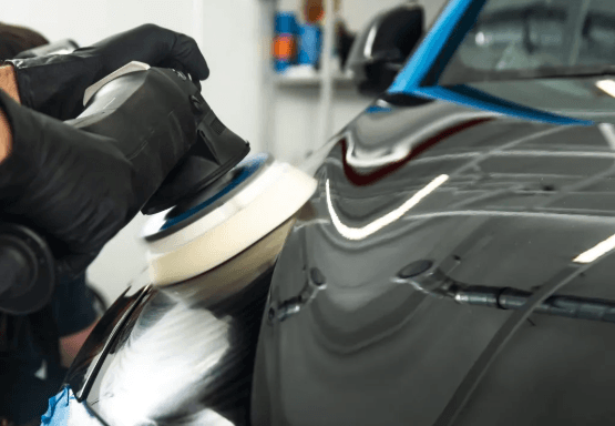 Detailer using a dual-action polisher on a dark vehicle panel, paint correction in progress